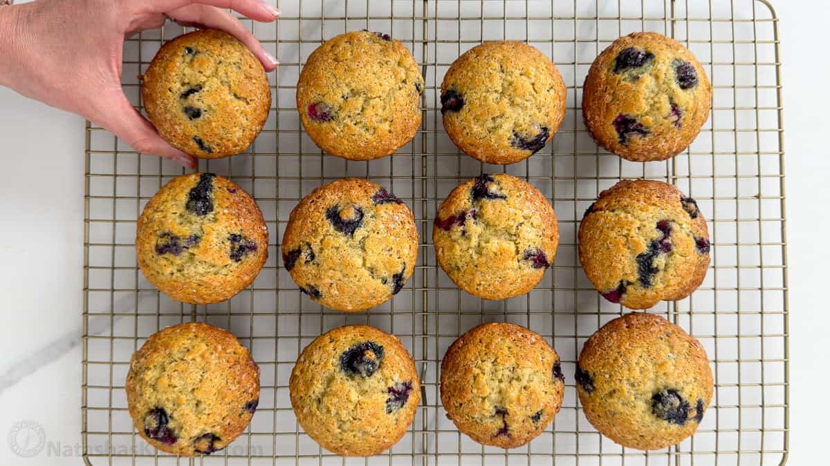 Easy Blueberry Banana Muffins bake up moist, tall, domed, and fluffy with great banana flavor and plenty of juicy blueberries. Hand removing a blueberry banana muffin from a cooling rack