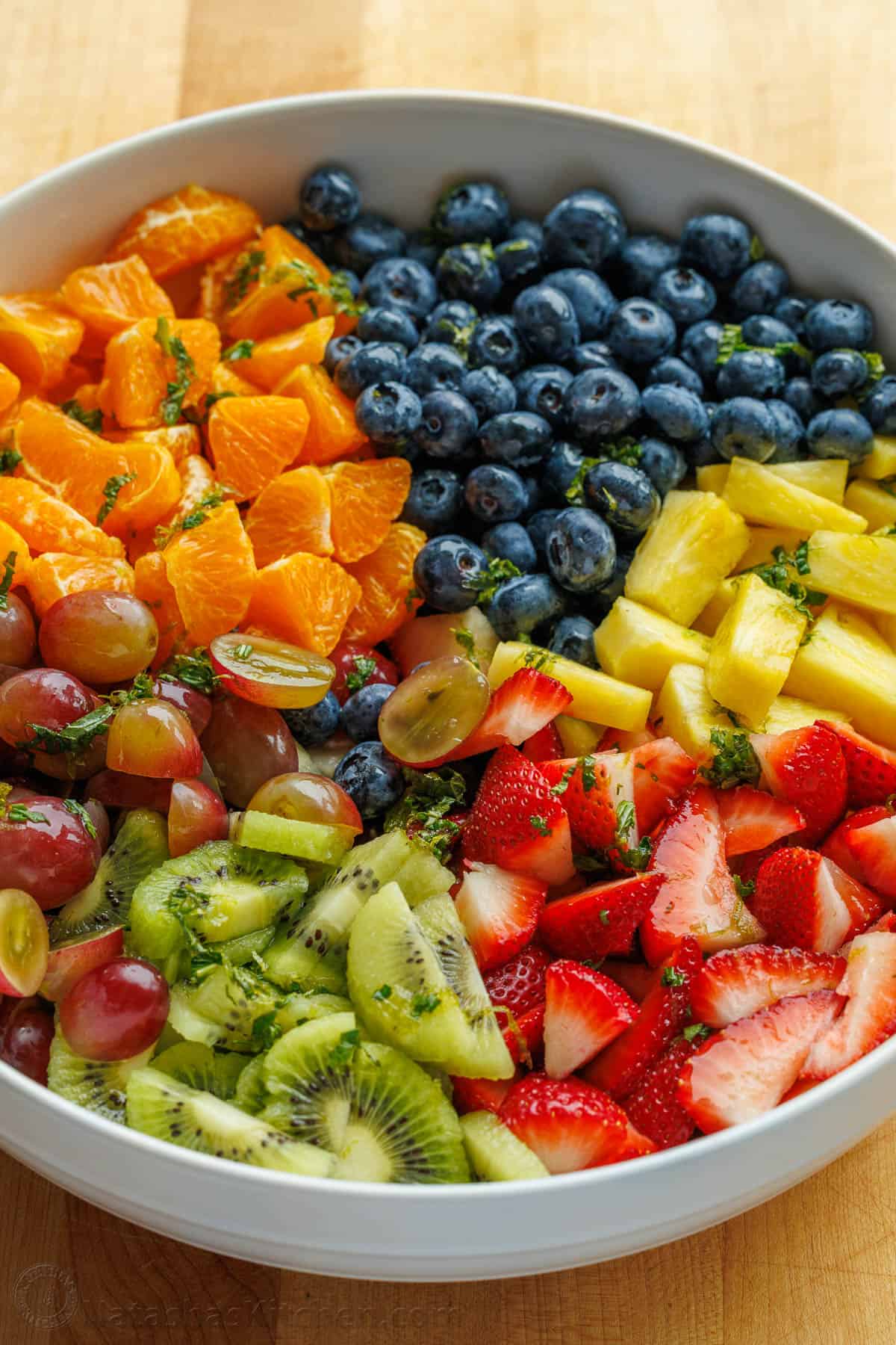 white serving bowl with mandarin oranges, blueberries, pineapple, strawberries, kiwi, and grapes.