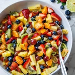 Fruit Salad dressed and served in a white bowl with a serving spoon