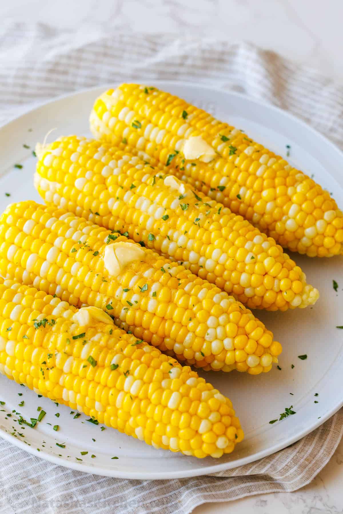 Boiled corn on the cob on a white serving tray with butter melting on top