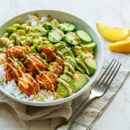 Healthy salmon rice bowl recipe with edamame, air fryer salmon, cucumbers and mayo sauce over a bed a rice in a white bowl