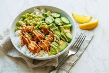 Healthy salmon rice bowl recipe with edamame, air fryer salmon, cucumbers and mayo sauce over a bed a rice in a white bowl