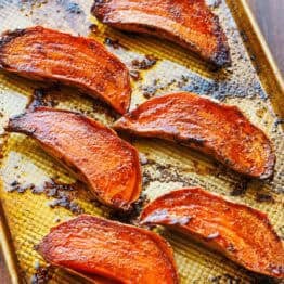 Tray of caramelized roasted sweet potato halves fresh out of the oven with crispy roasted sides.