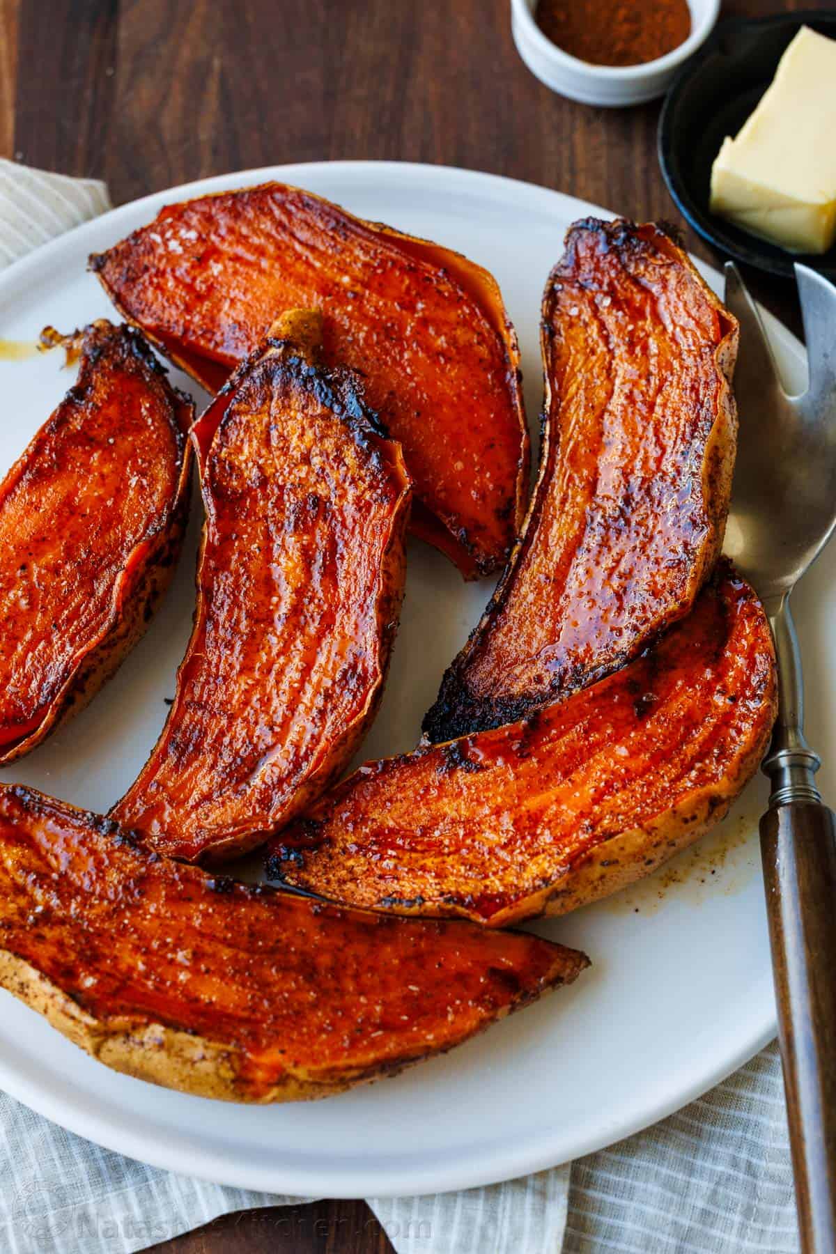 Caramelized roasted sweet potato halves side dish on a white plate with serving utensils