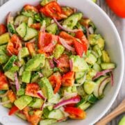 Cucumber tomato avocado salad mixed together and served in a white bowl