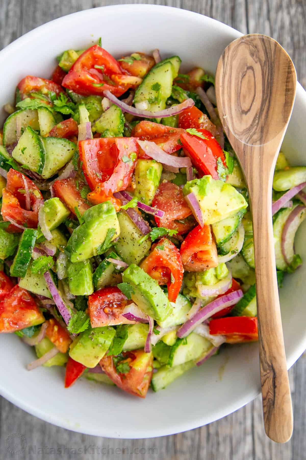 Mixed salad in a white bowl with serving spoon