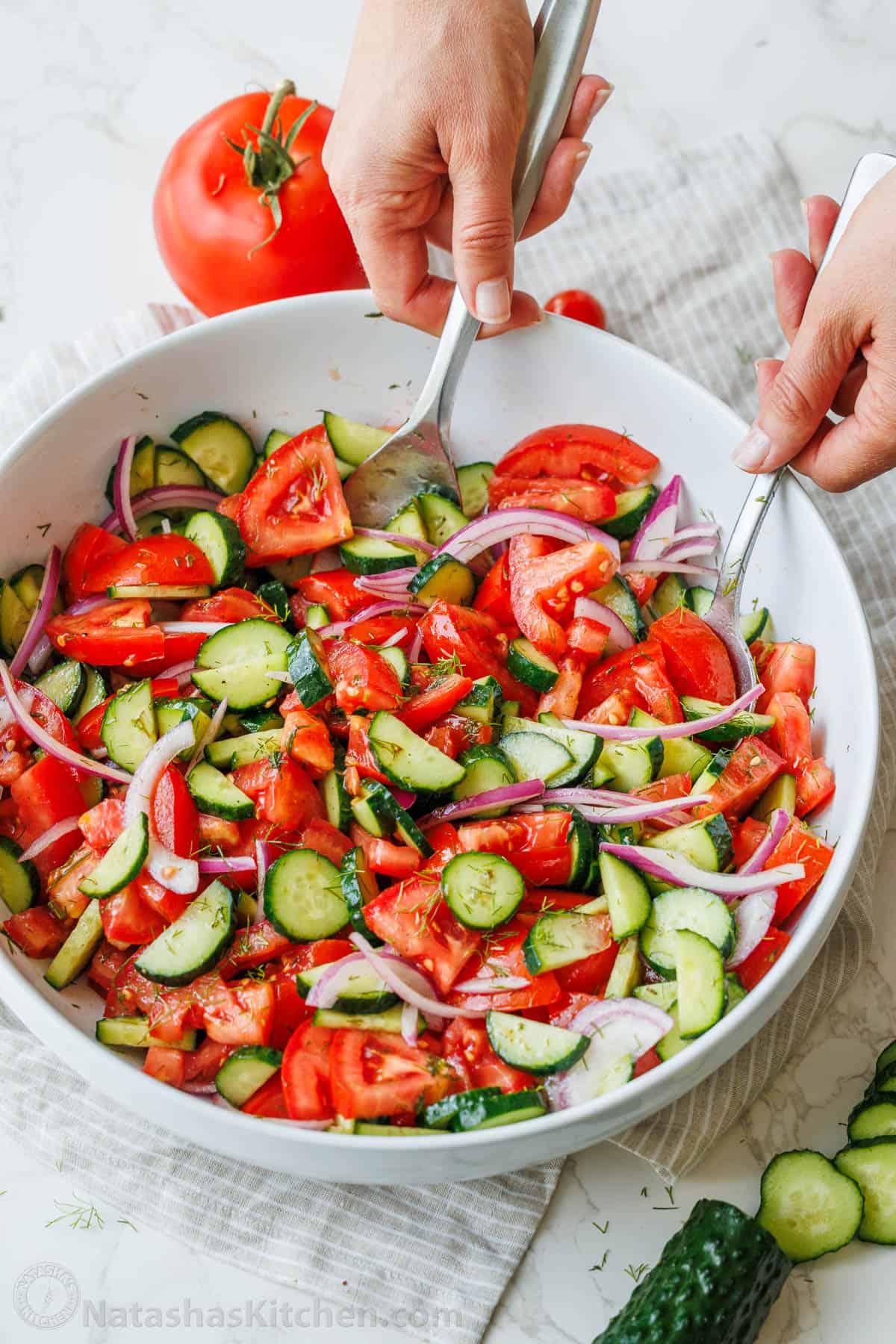 Tossed cucumber tomato salad in a white bowl with bright tomatoes, cucumbers, red onions and a fresh dill dressing