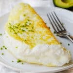Souffle style fluffy egg white omelette folded on a plate with chives to garnish and fork to eat.