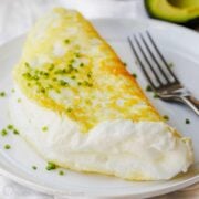 Souffle style fluffy egg white omelette folded on a plate with chives to garnish and fork to eat.