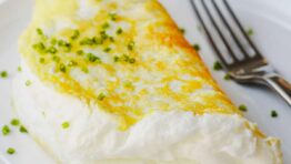 Souffle style fluffy egg white omelette folded on a plate with chives to garnish and fork to eat.