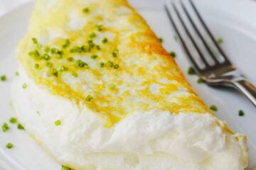 Souffle style fluffy egg white omelette folded on a plate with chives to garnish and fork to eat.