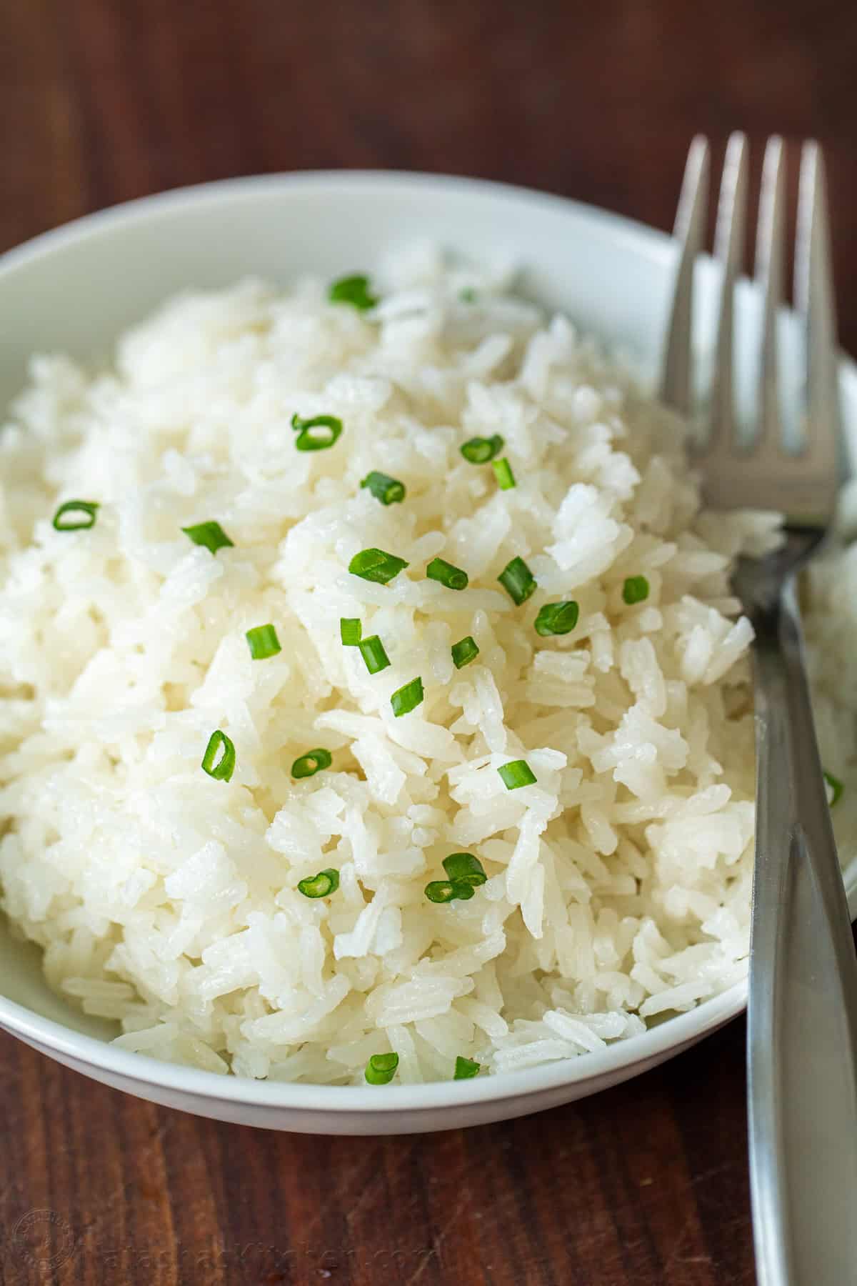 How to cook rice perfectly every time with the best rice-to-water ratio and a foolproof stovetop method for fluffy white rice. Get the recipe! Cooked rice in a white serving bowl garnished with chives