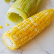 juicy microwaved corn on the cob with husk leaves in in the background