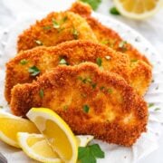 Crispy pork schnitzel on a white serving plate with lemon wedges