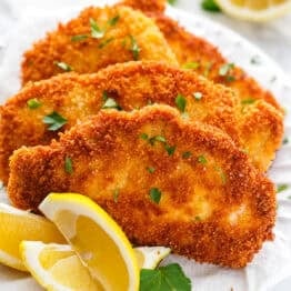 Pork schnitzel on a white plate garnished with parsley and lemon wedges