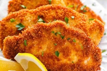 Pork schnitzel on a white plate garnished with parsley and lemon wedges
