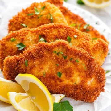 Pork schnitzel on a white plate garnished with parsley and lemon wedges