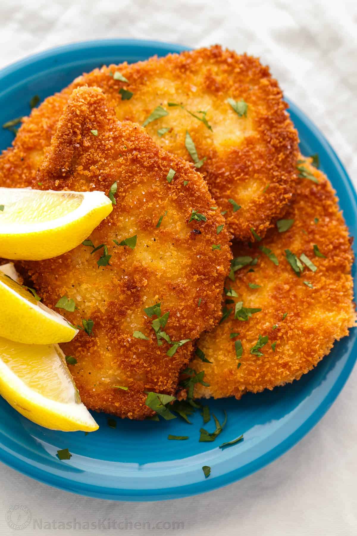 Crispy pork schnitzel arranged on a blue plate with lemon wedges