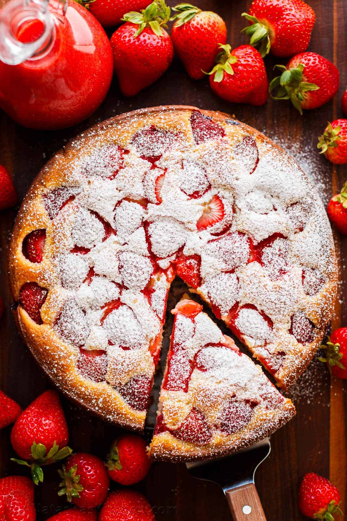 Easy Strawberry Cake is soft, moist, and loaded with fresh strawberries. Serve it with a simple 2-ingredient strawberry sauce. Easy Strawberry cake with a slice cut out surrounded by fresh strawberries