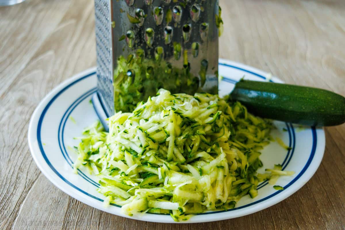 grated fresh zucchini on a white plate with a box grater