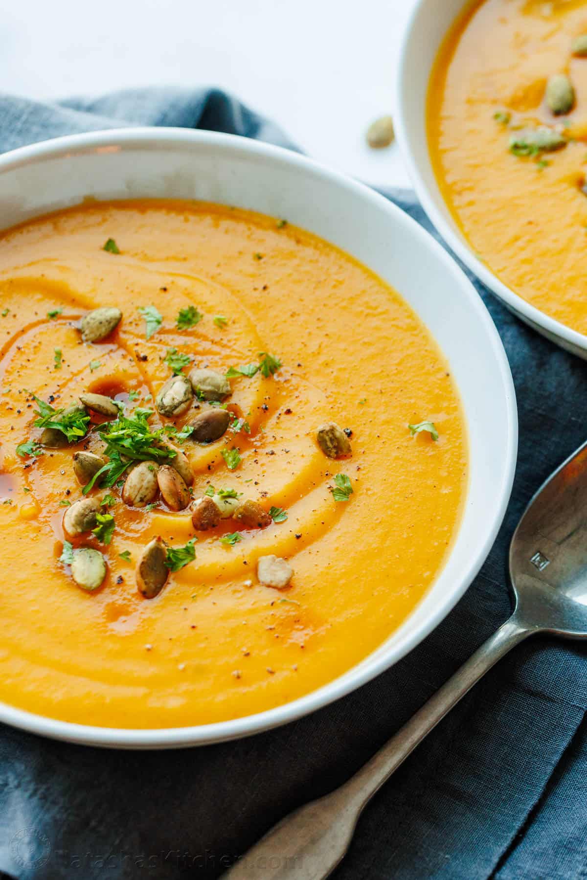 Easy Butternut Squash Soup recipe made from roasted butternut squash that's blended into a creamy soup and topped with maple syrup and bacon. Roasted Butternut squash soup in a white serving bowl with spoon