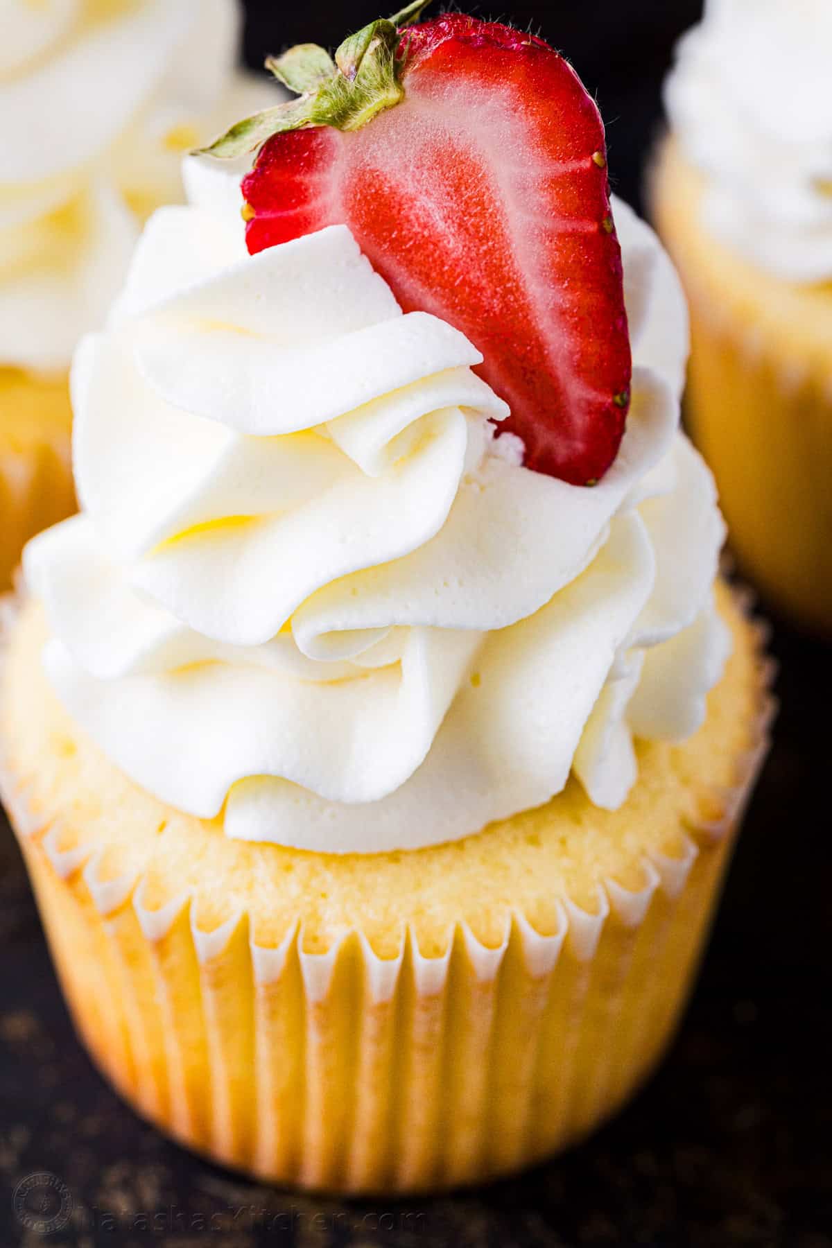 This easy cupcake frosting is light, fluffy, and not too sweet. Made with 5 ingredients, it pipes beautifully onto cupcakes and cakes. Cupcake frosting garnished with a strawberry
