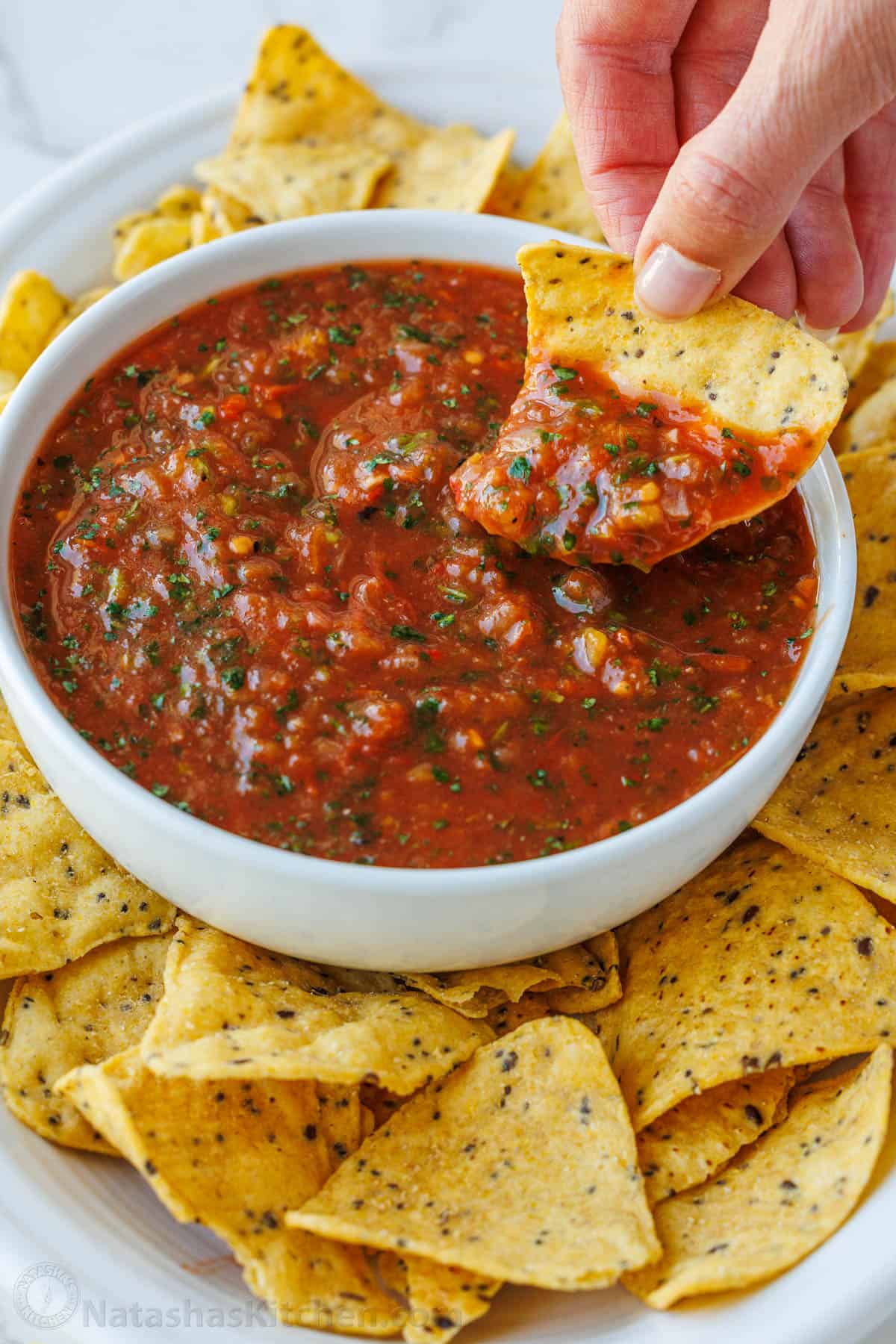 Easy Roasted tomato Salsa with smoky fire-roasted flavor, fresh cilantro, and a scoopable texture. Freezer-friendly and better than store-bought. Scooping roasted tomato salsa from a small bowl with more chips surrounding