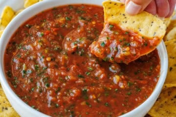 chip scooping roasted tomato salsa from a white bowl