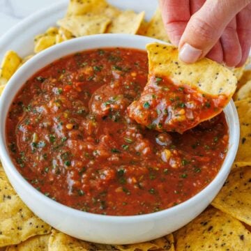 chip scooping roasted tomato salsa from a white bowl