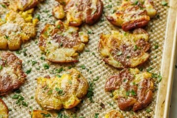 sheet pan of crispy smashed potatoes lined up with parsley garnish