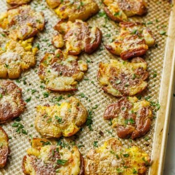 sheet pan of crispy smashed potatoes lined up with parsley garnish