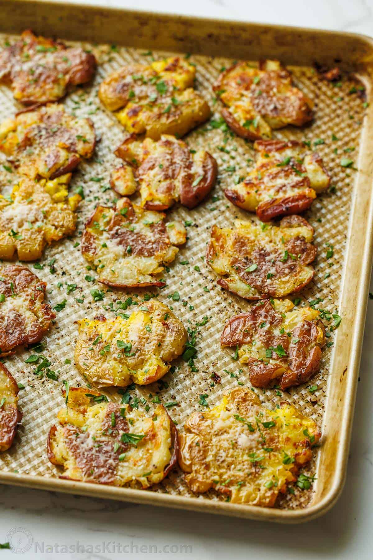 sheet pan of crispy smashed potatoes lined up with parsley garnish