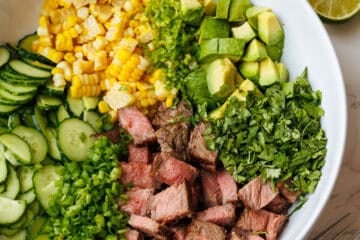 steak salad divided into ingredients in a white bowl with honey lime dressing in a mason jar on the side