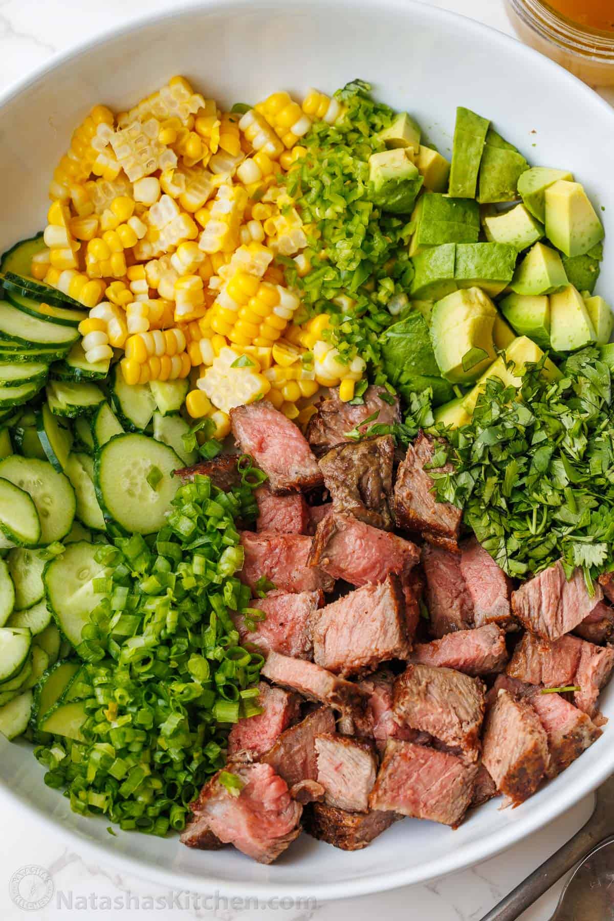 Steak Salad recipe with pan-seared steak, cucumber, corn, avocado, cilantro, and jalapeño, tossed with a vibrant honey-lime dressing. Steak salad recipe divided in a white bowl