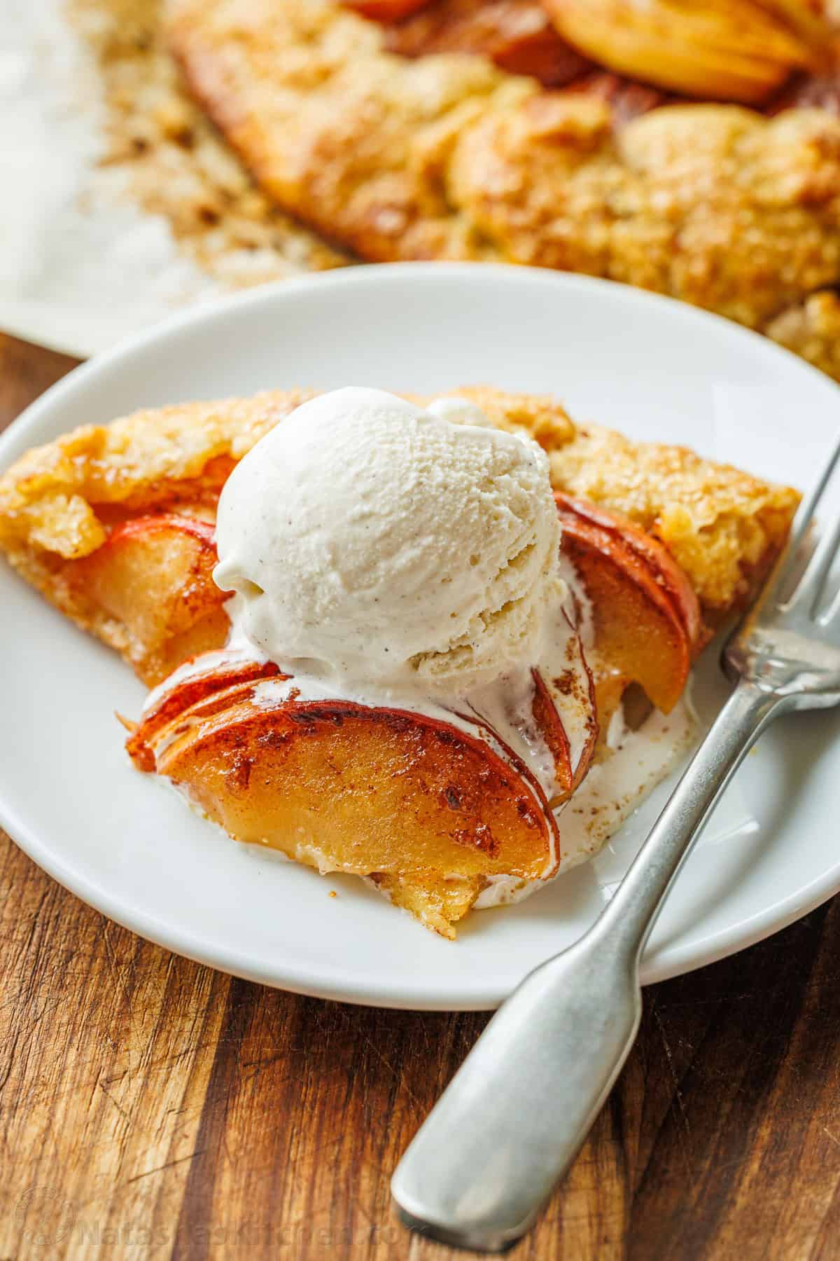 Easy Apple Galette with a flaky homemade crust and cinnamon apples. No pie plate or peeling needed for this beautiful rustic fall dessert. slice of apple galette on a white plate with scoop of vanilla ice cream on top