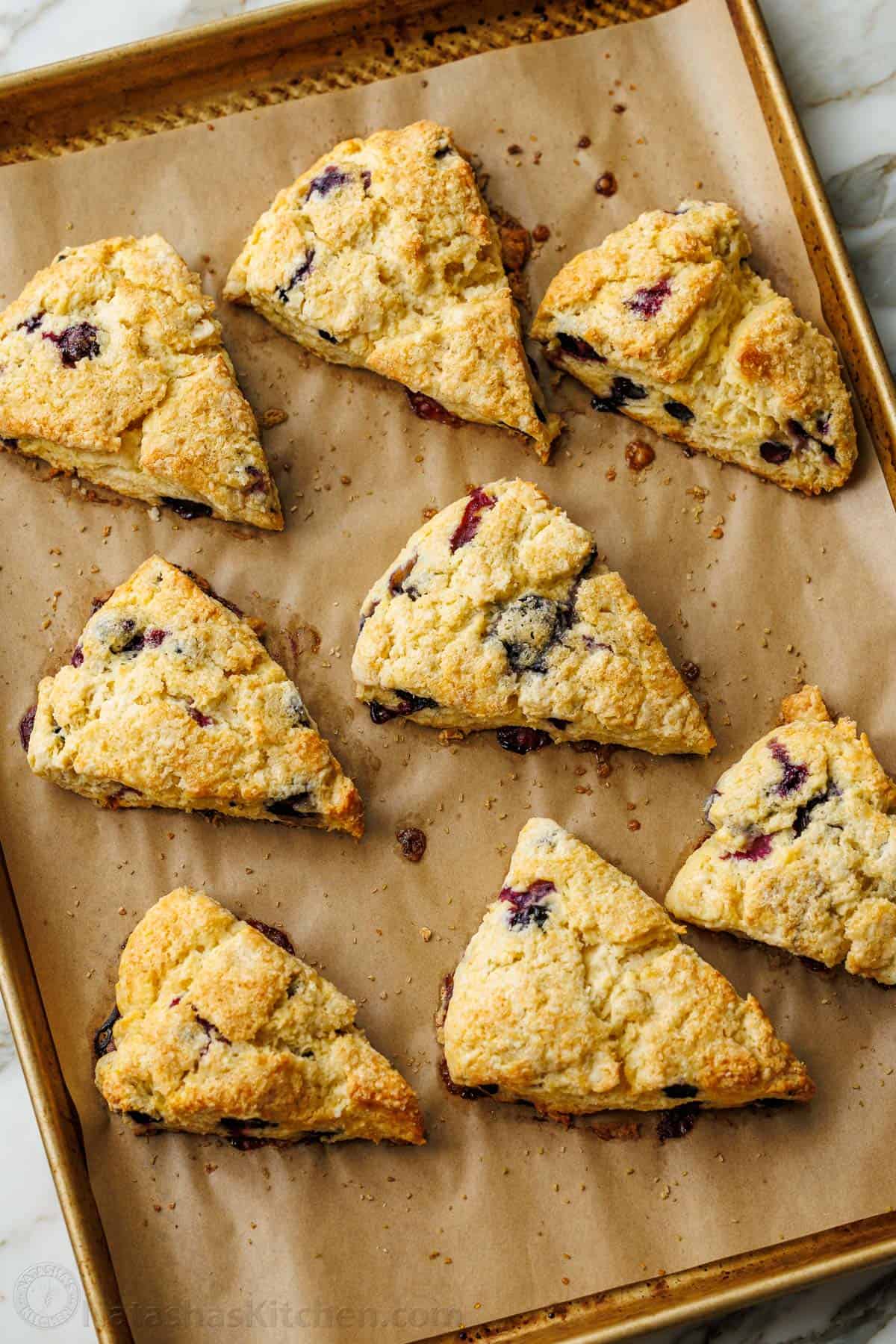 These easy Blueberry Scones are buttery, flaky, packed with juicy blueberries, and finished with a bright lemon glaze. Make-ahead friendly, too. Blueberry Scones baked up on a baking sheet