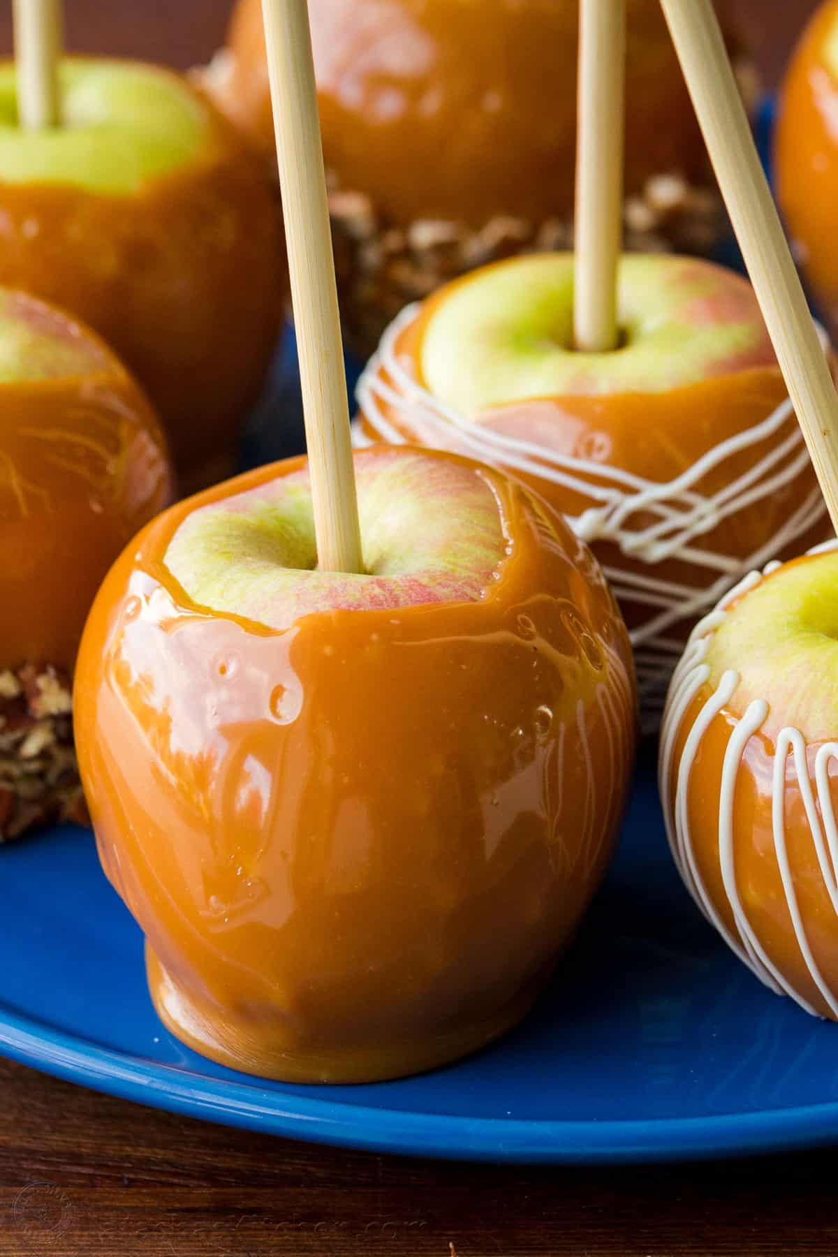 Homemade Caramel Apples are such a fun treat for Fall. This caramel apple recipe is so easy with only 3 ingredients for the caramel dip. Homemade Caramel apple on a platter with more coated apples