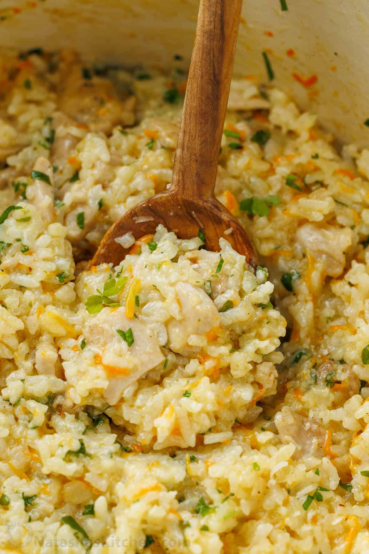 Wooden spoon scooping creamy chicken and rice from a pot