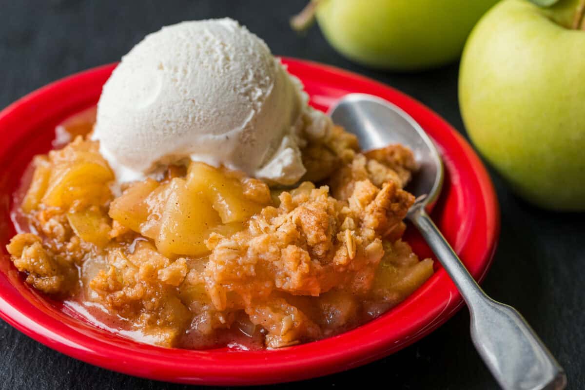 Apple crisp served on red plate with a scoop of vanilla ice cream
