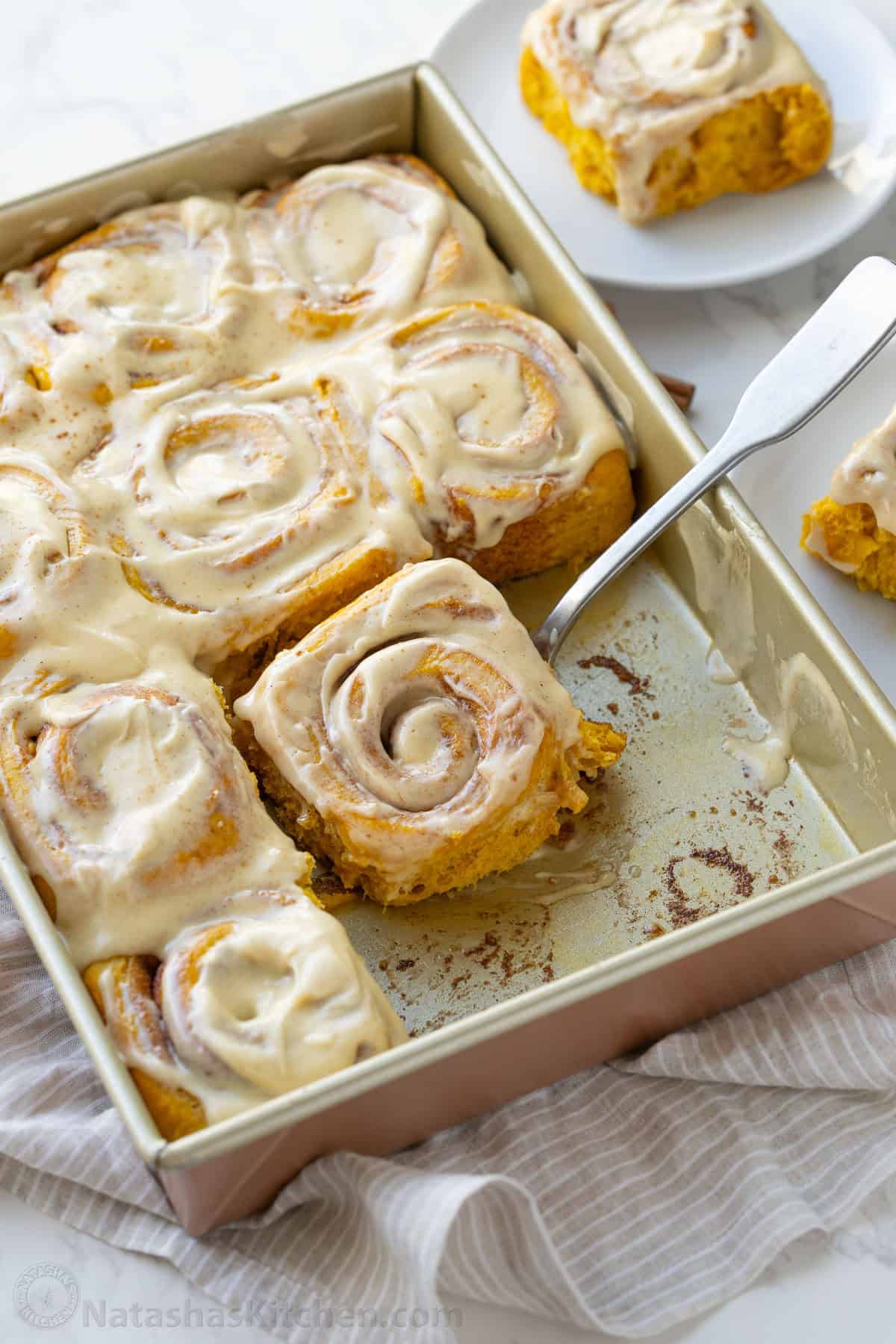 Serving a pumpkin cinnamon roll with icing from a rectangle baking dish