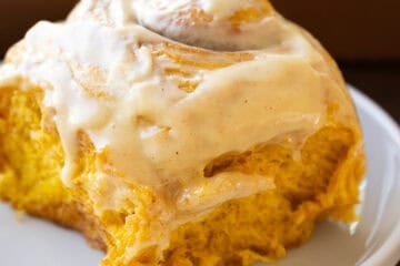Close up of a pumpkin cinnamon roll on a white plate with icing and a fork to eat with