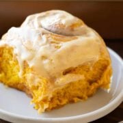 single Pumpkin cinnamon roll on a white plate with dripping frosting on top