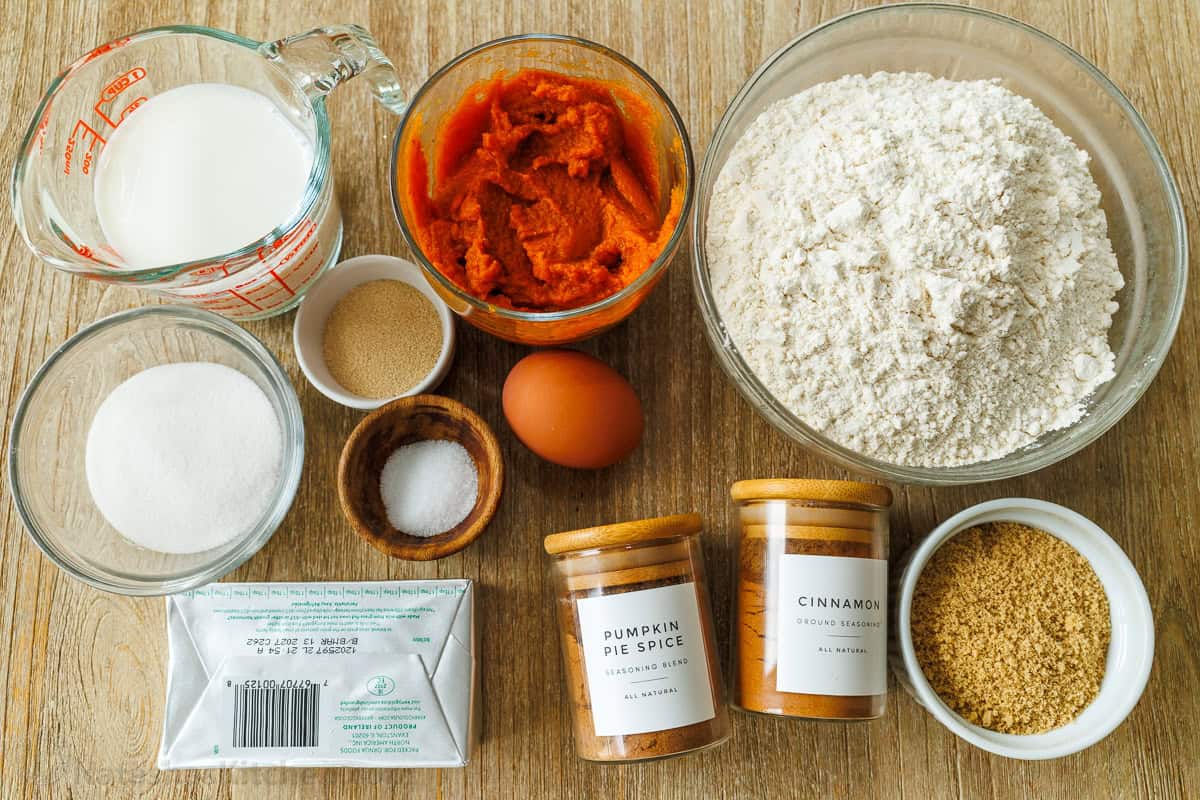 ingredients for pumpkin cinnamon rolls with milk, yeast, pumpkin puree, sugar, flour, egg, butter, pumpkin pie spice, and brown sugar