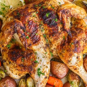 Spatchcock Chicken roasted on a baking sheet with potatoes, carrots and Brussels sprouts.