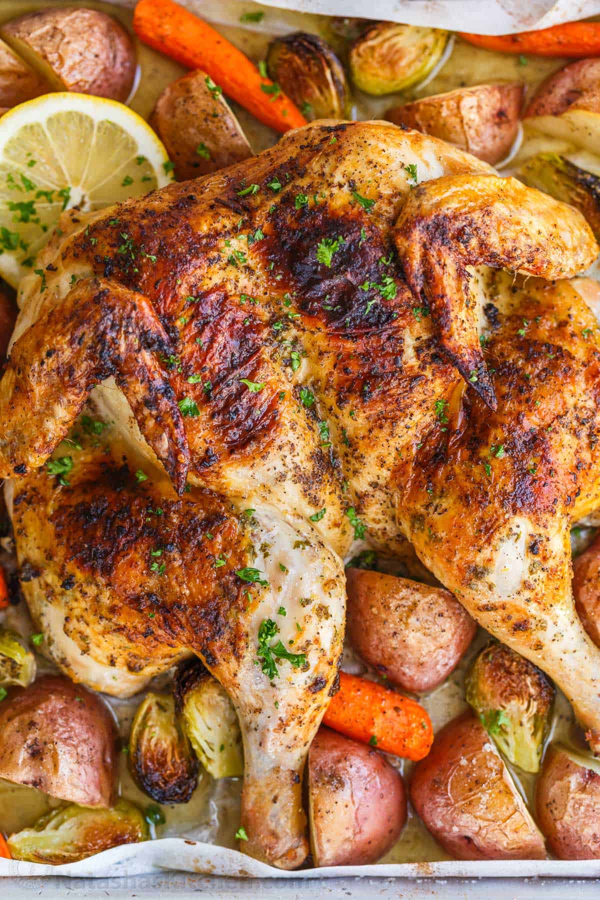 Easy Spatchcock Chicken with juicy meat, crispy skin, and garlic-herb butter. Roast it with vegetables for a simple one-pan dinner. Spatchcock Chicken roasted on a baking sheet with potatoes, carrots and Brussels sprouts.