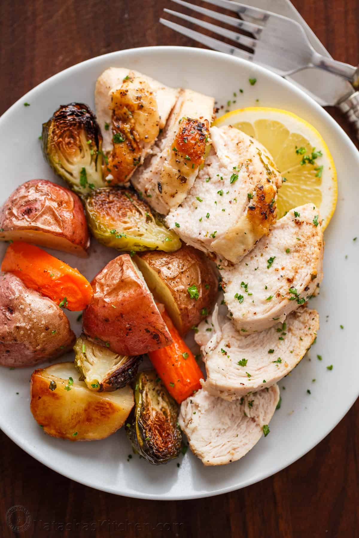 Easy Spatchcock Chicken with juicy meat, crispy skin, and garlic-herb butter. Roast it with vegetables for a simple one-pan dinner. Sliced juicy chicken breast from spatchcock chicken served with roasted vegetables on white plate