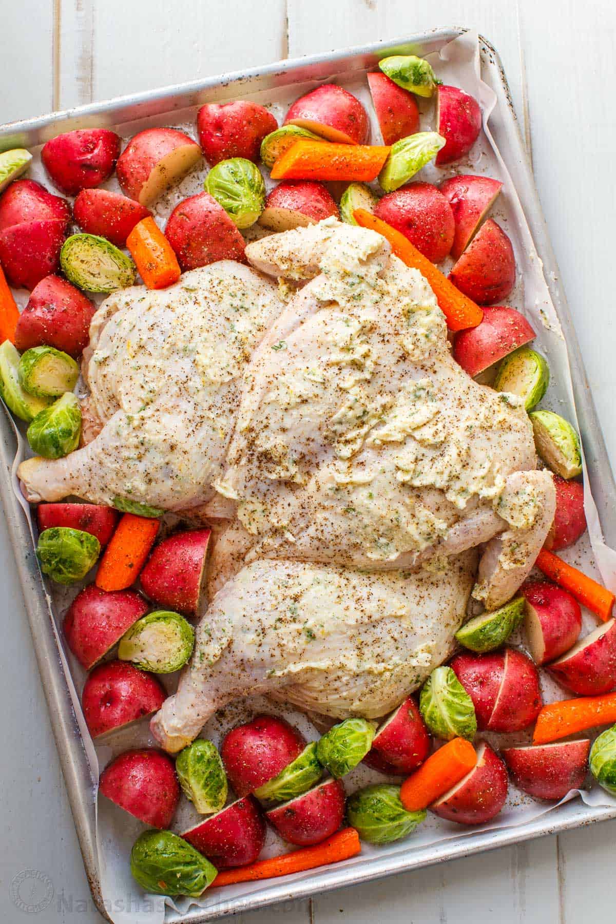 Easy Spatchcock Chicken with juicy meat, crispy skin, and garlic-herb butter. Roast it with vegetables for a simple one-pan dinner. Spatchcocked chicken prepped on a baking sheet ready for roasting