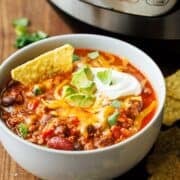 Instant Pot chili in a white bowl topped with cheddar, sour cream, avocado, cilantro and a tortilla chip