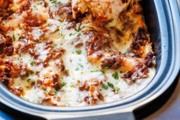 Serving spatula lifting a slice of lasagna out of an oval slow cooker