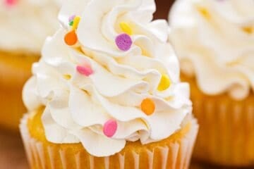 Swiss meringue buttercream piped in a tall swirl on a vanilla cupcake with confetti sprinkles.